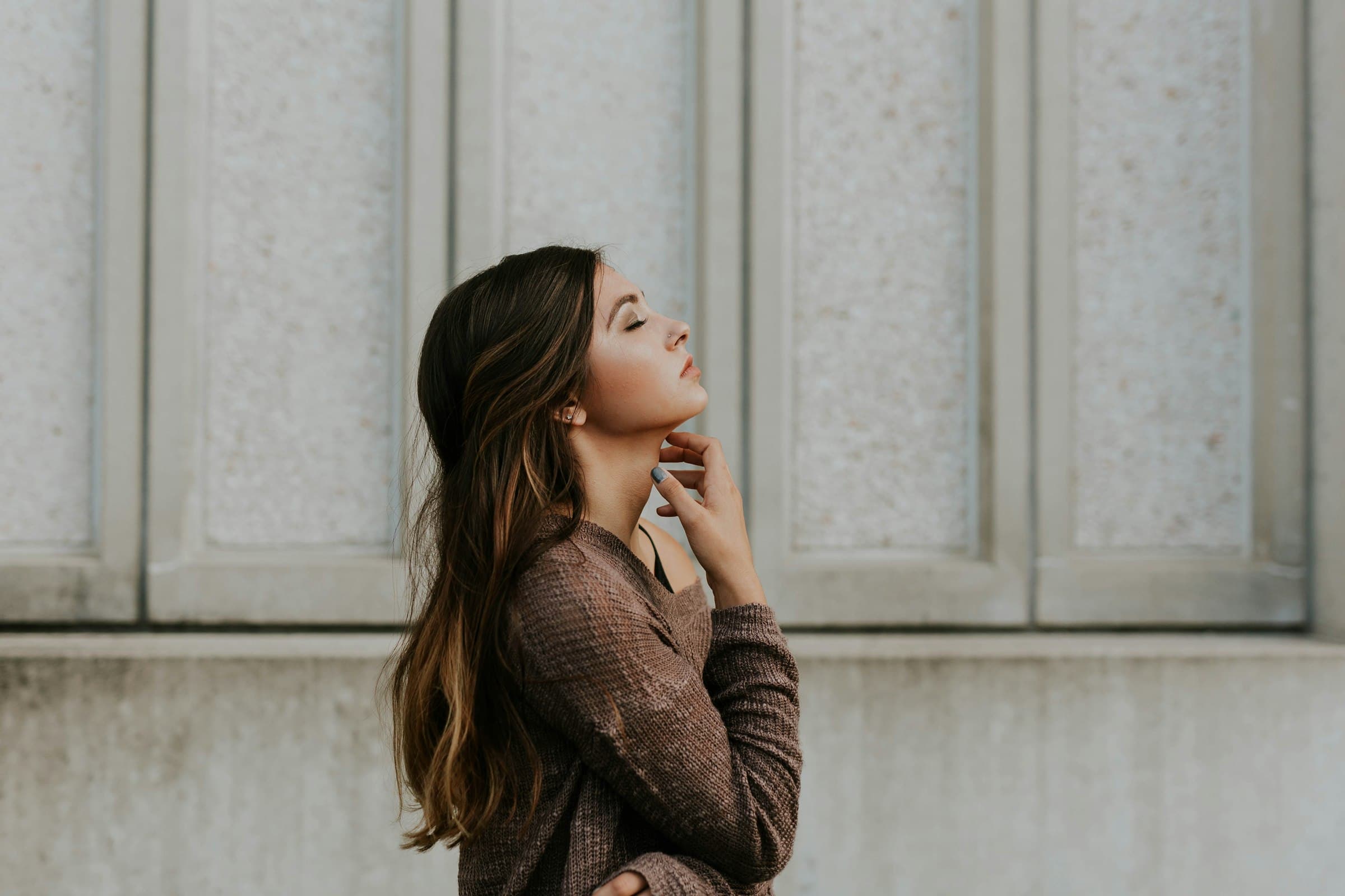 Mulher de perfil com os olhos fechados, em um momento de calma diante de uma parede de pedra
