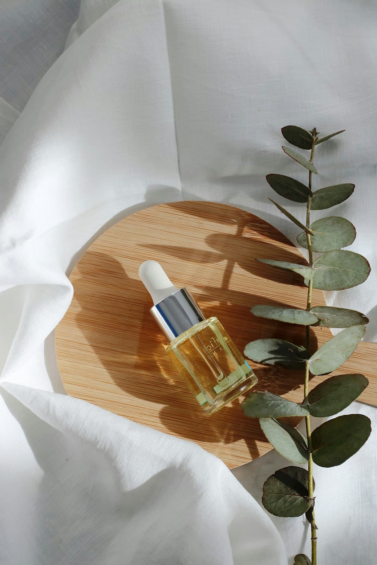 Frasco de sérum sobre madeira clara, entre folhas verdes